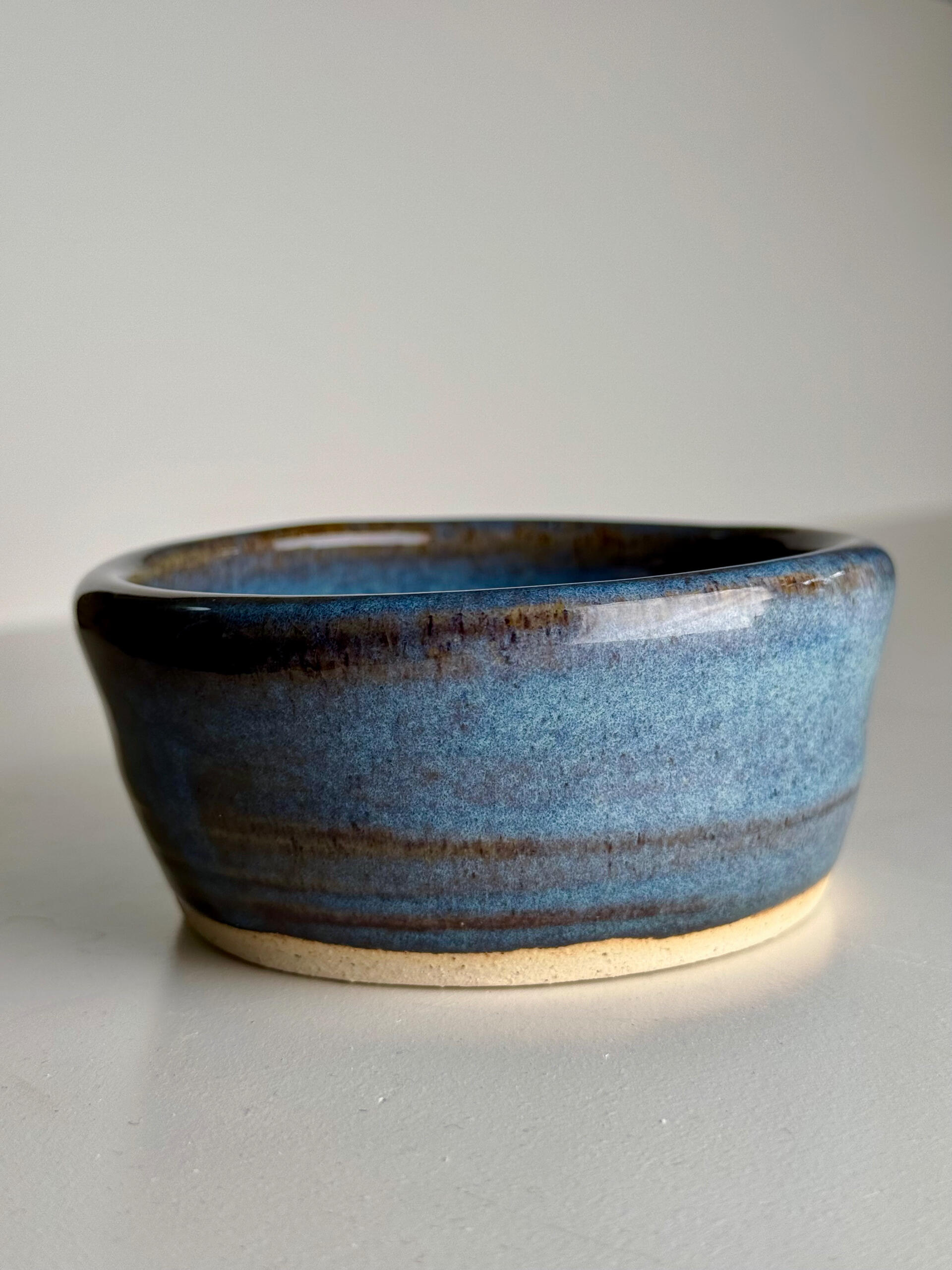 Blue Gradient Bowl Small handmade ceramic bowl with flowing blue glaze over natural clay base, sitting on a white surface