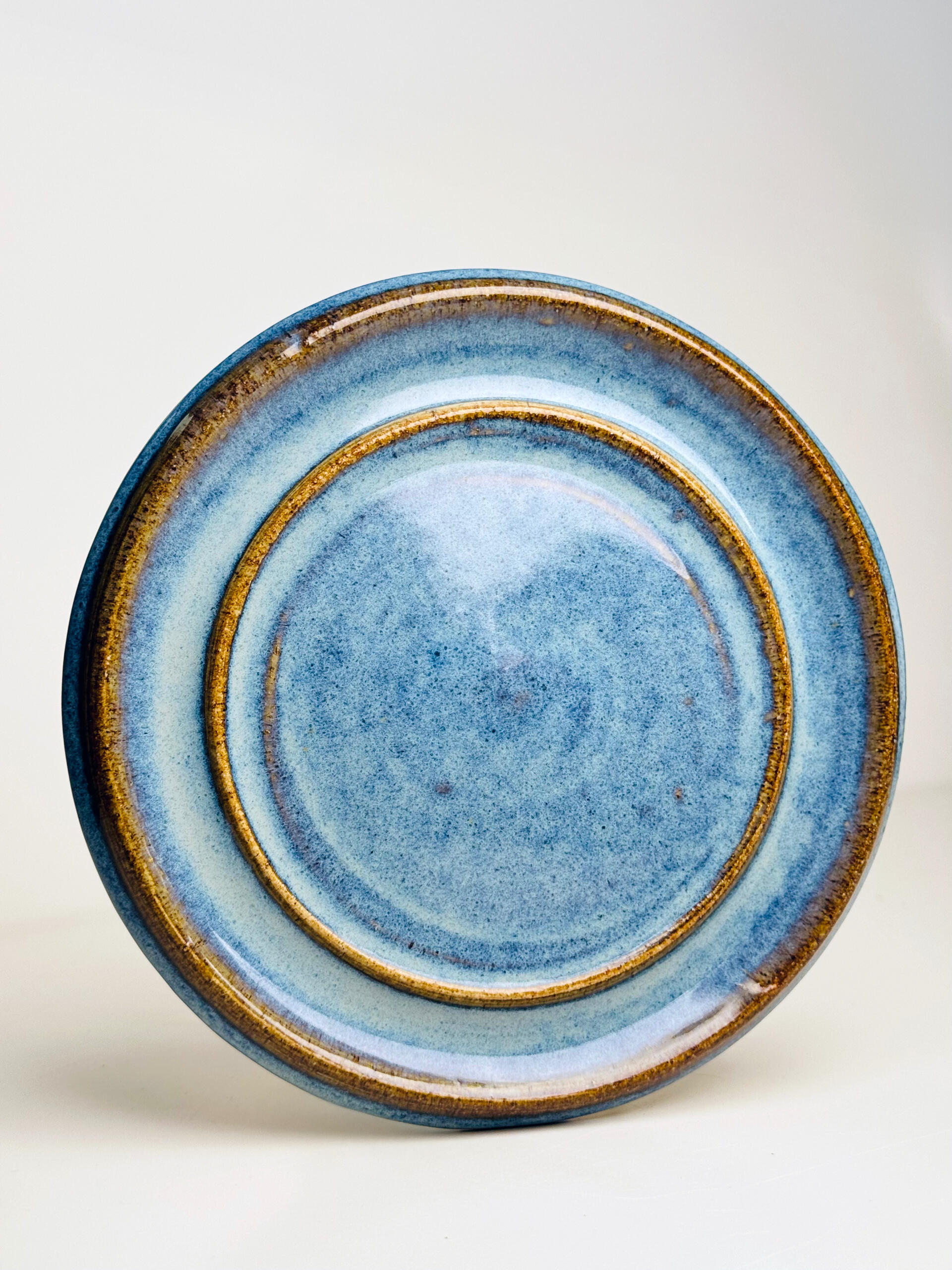 Blue Rim Stoneware Plate Small handmade ceramic plate with flowing blue glaze over natural clay base, sitting on a white surface