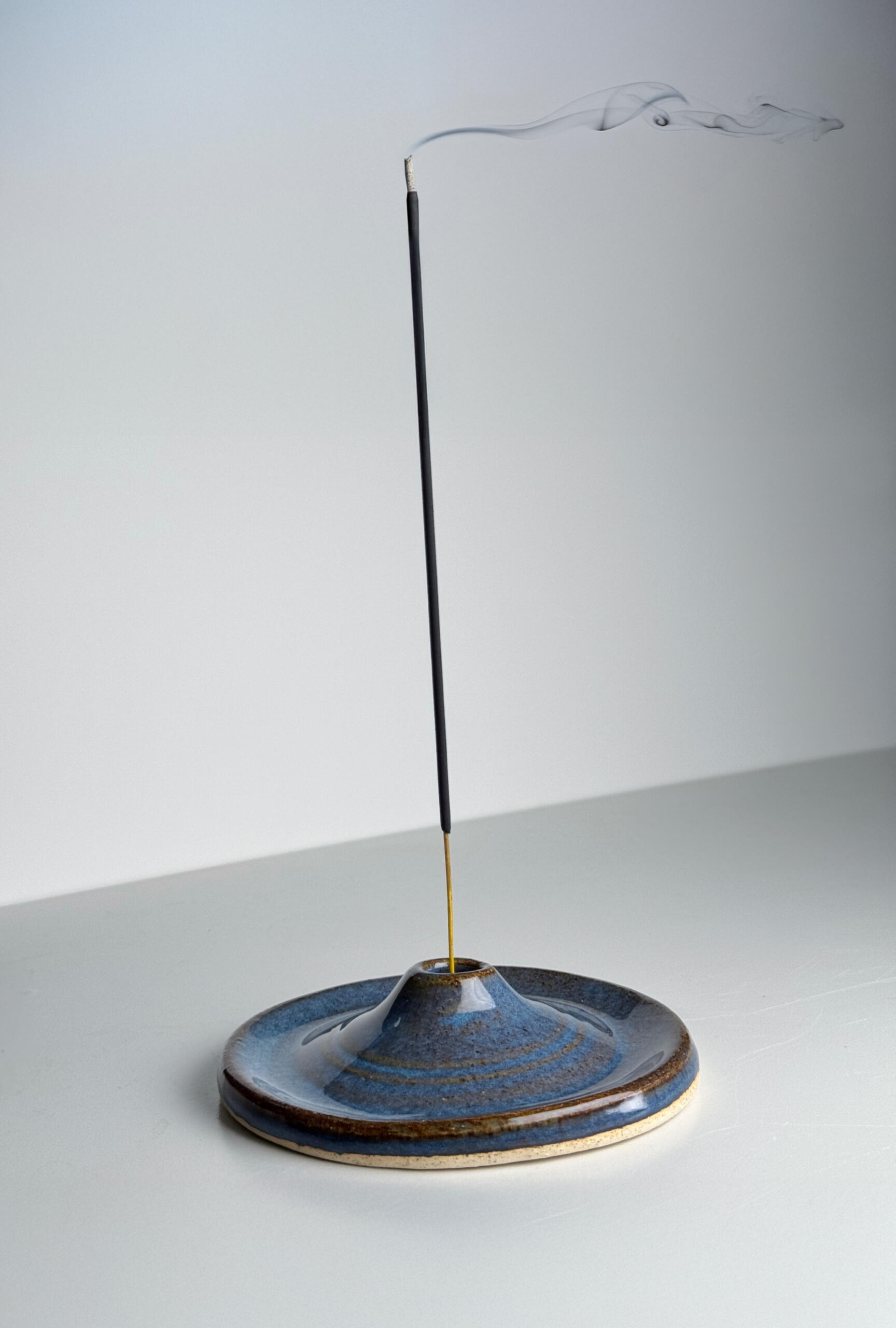 Blue Incense Holder Small handmade incense holder with flowing blue glaze over natural clay base, sitting on a white surface