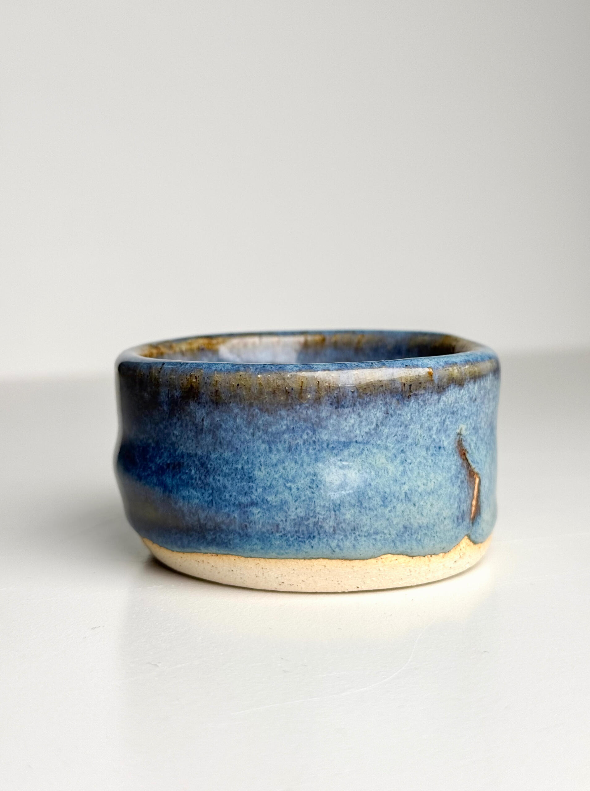 Blue Gradient Cup Small handmade ceramic cup with flowing blue glaze over natural clay base, sitting on a white surface