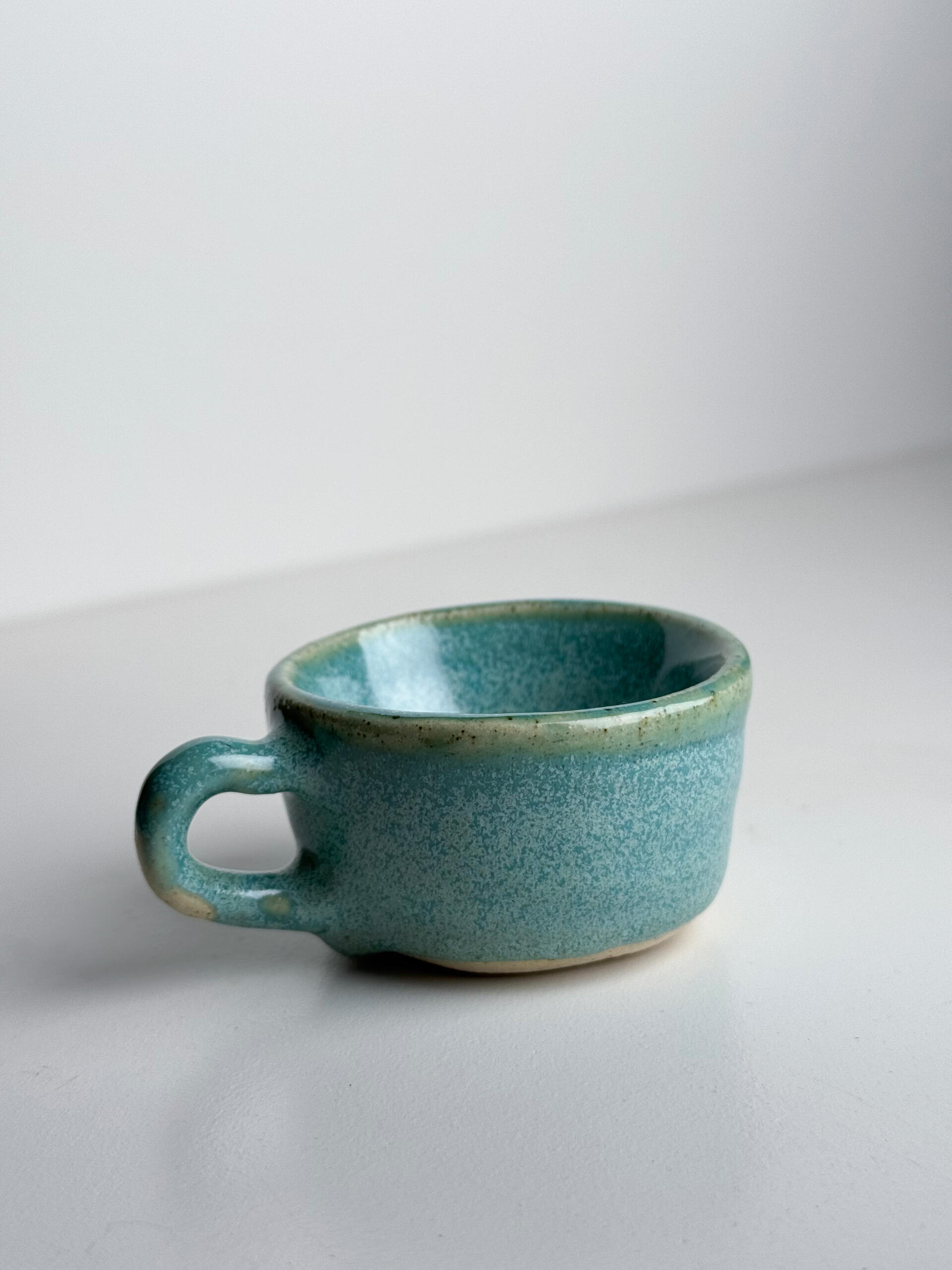 Green-Blue Gradient Cup Small handmade ceramic cup with flowing green-blue glaze over natural clay base, sitting on a white surface